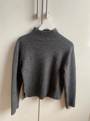 Mörkgrå stickad tröja Gina Tricot - Mysig mörkgrå stickad tröja från Gina Tricot med hög krage och ribbade muddar. Tröjan har en rak, något kortare passform och långa ärmar.