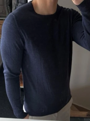 Mörkblå tröja från J.Lindeberg - Snygg mörkblå tröja från J.Lindeberg i tunn, mjuk ullmix. Tröjan har rund halsringning och långa ärmar, perfekt för lager på lager eller som den är. Enkel och stilren design som passar till det mesta. Storlek m men har krympt så sitter som xs/s