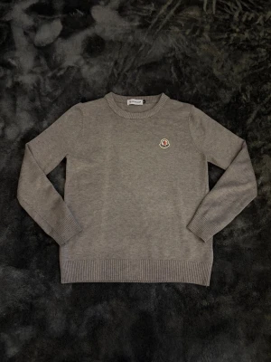 Grå stickad tröja från Moncler - Snygg grå stickad tröja från Moncler med rund halsringning och diskret Moncler-logga på bröstet. Storlek M men passar S.