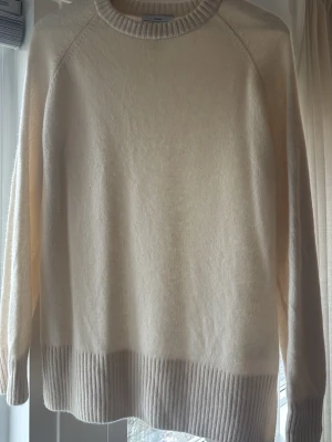 Beige stickad tröja från Filippa K - Klassisk beige kashmir tröja från Other stories med rund halsringning och ribbade muddar vid ärmslut och nederkant. Tröjan har en avslappnad passform och är tillverkad i mjukt material, perfekt för lager på lager. Har liten slita på båda sidor 