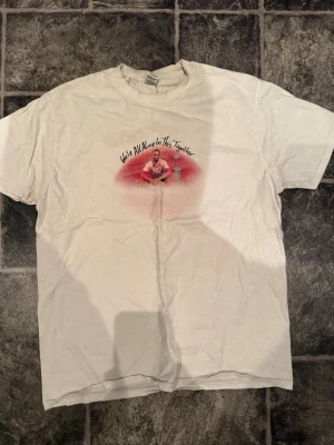 Dave were all alone in this togheter merch  - Vit t-shirt med ett tryck på bröstet som föreställer en person och texten 'We're All Alone In This Together' ovanför. Klassisk passform med rund hals och korta ärmar. Perfekt för en avslappnad stil. DAVE MERCH