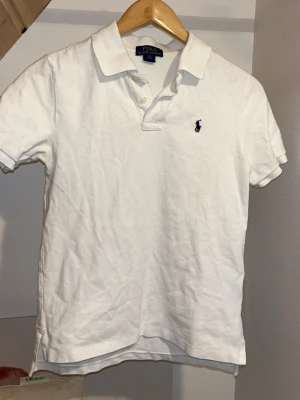 Vit pikétröja från Polo Ralph Lauren - Klassisk vit pikétröja från Polo Ralph Lauren med korta ärmar. Tröjan är storlek M men passar xs bäst. Kontakta vid minsta fundering