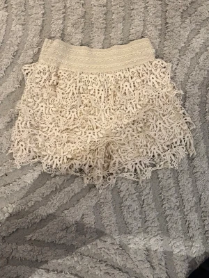 Vita shorts med volang - Säljer ett par vita virkade shorts med bred resår i midjan och flera lager volangdetaljer. Perfekta för sommaren. Skit snygga och trendiga.