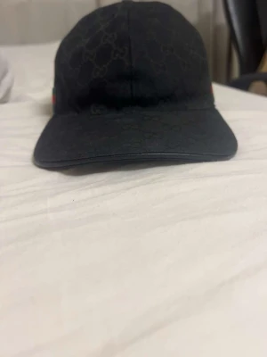 Svart Gucci keps med monogram - Säljer en svart keps från Gucci med klassiskt GG-monogram över hela kepsen. På sidan finns en grön och röd rand som ger den en ikonisk look. Justerbar rem baktill för perfekt passform. Materialet känns slitstarkt och exklusivt.                      Pris kan diskuteras vid snabbäffar!! Kvitto o dustbag ingår!!  Möts i Stockholm!!