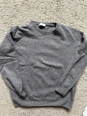 Grå stickad tröja Filippo Riberti - Mjuk och stilren grå stickad tröja från Filippo Riberti. Tröjan har rund halsringning, långa ärmar och ribbade muddar vid ärmslut och nederkant. Perfekt för lager-på-lager och enkel att matcha med jeans eller kjol.