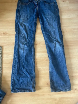 Blå raka jeans med fickor - Säljer ett par klassiska blå jeans med raka ben och normal midja. Jeansen har fram- och bakfickor samt kontrastsömmar. Materialet är denim i bomull och passformen är avslappnad. Perfekta för en avslappnad och stilren look.