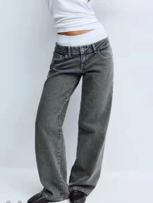 Grå baggy jeans med ultra låg midja - Prislapp sitter kvar!Säljer ett par gråa baggy jeans med låg midja och raka, vida ben. Jeansen har klassiska fem fickor och synliga sömmar. Perfekta för en avslappnad och trendig look. Materialet är denim i bomull.