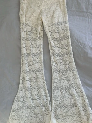 Vita utsvängda spetsleggings - Superfina vita leggings i genombruten spets med blommönster och utsvängda ben. Perfekta för dig som vill sticka ut med en romantisk och trendig look. Materialet är stretchigt och följsamt för en bekväm passform. Står ingen storlek eller vart den kommer ifrån men skulle nog säga XS.