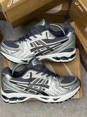 ASICS silvriga sneakers med mesh - Snygga sneakers från ASICS i silver och svart med detaljer i vitt och grönt. Ovandelen är i mesh och syntetmaterial för bra andningsförmåga och komfort. Klassisk ASICS-logga på sidan och robust sula med dämpning. Perfekta för en sportig och trendig look.