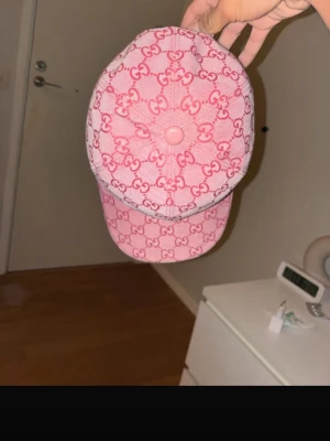 Gucci Dubai keps - Säljer en rosa keps från Gucci med klassiskt GG-monogram i en mörkare rosa nyans. Kepsen har böjd skärm och är tillverkad i tygmaterial. Perfekt accessoar för att lyfta din outfit med en lyxig touch.