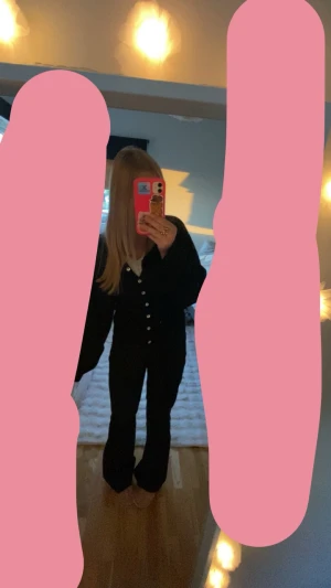 Svart kofta med knappar från Gina Tricot - Säljer en svart kofta från Gina Tricot med v-ringning och vita knappar framtill. Koftan har lång ärm och bred ribbstickad nederkant som ger en snygg passform. Perfekt att styla över ett linne eller t-shirt.