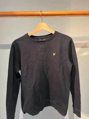Lyle and Scott tröja  - Svart Lyle and Scott tröja med en gul broderad fågel på bröstet. 