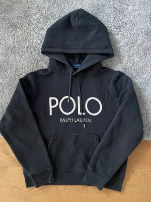 Svart hoodie från Polo Ralph Lauren - Svart Polo Ralph Lauren hoodie i storlek M säljes. I mycket bra skick och utan defekter. Stilren hoodie med stort Polo Ralph Lauren tryck framtill och mjuk insida för extra komfort.  ✅ Storlek M ✅ Mycket bra skick ✅ Inga defekter ✅ Snabb frakt  Hör gärna av er vid frågor eller om ni vill ha fler bilder! Dam