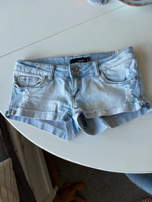 Ljusblå lågmidjade jeansshorts från Tally weijl - Snygga ljusblå lågmidjade jeansshorts från True Well med slitna detaljer och klassisk femficksdesign. Shortsen har låg midja, bälteshällor och knappstängning.