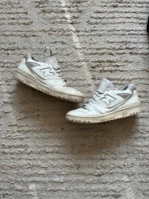 Vita New Balance sneakers i läder - Snygga vita sneakers från New Balance med klassisk siluett och lågt skaft. Skorna är tillverkade i läder med perforerade detaljer på sidorna och har en robust sula. Perfekta för en clean och sportig look.