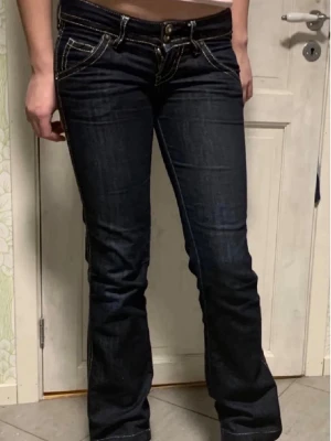 Mörkblå bootcut jeans från Guess - Jag säljer ett par lågmidjade mörkblå bootcut jeans som är äkta Guess i storlek 27 i jeans storlek så passar någon dom har storlek 34-36. Från gylf till skrev är det 15 cm så de är väldigt lågmidjade. Innerbenslängden är 76 cm. Mycket bra skick. 