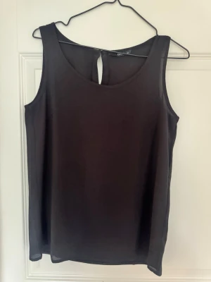 Svart ärmlös topp från ONLY - Snygg svart ärmlös topp från ONLY med rund halsringning och knappdetalj i nacken. Tillverkad i ett lätt och mjukt tyg som ger en skön känsla. Perfekt att matcha med jeans eller kjol för en stilren look.