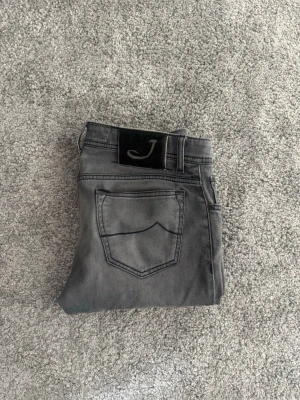 Jacob Cohen jeans  - Snygga grå jeans från Jacob Cohen i slim fit-modell. Jeansen har klassisk femficksdesign, svarta detaljer och en svart patch med J-logga bak i midjan. Perfekta för dig som gillar stilrena och moderna jeans i mjukt denimtyg.