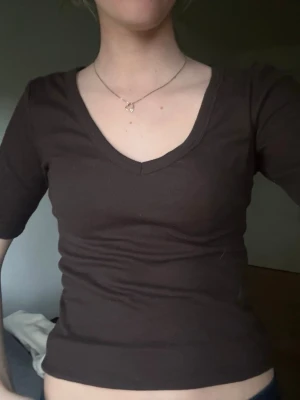 Brun v-ringad topp med kort ärm - Mörkbrun topp med v-ringning och korta ärmar. Toppens material känns mjukt och stretchigt, perfekt för en enkel och stilren look. Passformen är slim och modellen är klassisk utan mönster eller extra detaljer.