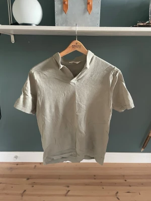 Beige pikétröja från H&M - Snygg beige pikétröja från H&M med korta ärmar och klassisk krage utan knappar. Tillverkad i ett mjukt och lätt material som passar perfekt till sommaren. Enkel och stilren design som är lätt att matcha med andra plagg. Endast testad