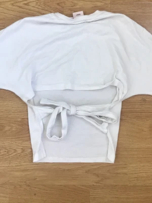 Vit omlottopp med knytband - Snygg vit topp från Nelly med knytband i midjan/baksidan. Toppen har korta ärmar och tight vid magen.