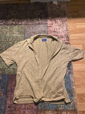 Beige skjorta från Jack & Jones - Säljer en beige skjorta från Jack & Jones med kort ärm och snyggt mönster i tyget. Skjortan har knappar framtill och är tillverkad i bomull, perfekt för en avslappnad stil.