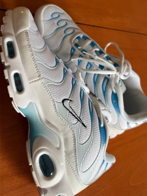 Nike Air Max Plus vita/blå sneakers - (( Använda 1 gång))Nike Air Max Plus sneakers i vitt mesh med blå detaljer och svarta swoosh-loggor. Skorna har synliga Air Max-enheter i sulan och vågformade mönster på ovandelen. Klassisk snörning och bekväm dämpning, perfekt för dig som gillar sportig och fräsch stil.