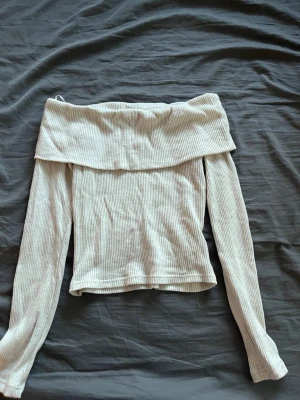 Off shoulder ribbad tröja vit - Trendig off shoulder tröja i ribbat vitt tyg. Långärmad modell med bred krage som vilar över axlarna. Perfekt för en stilren och avslappnad look. Materialet är mjukt och stretchigt för extra komfort.