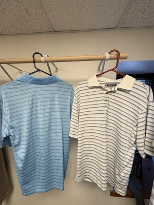 Två randiga pikétröjor från pebble beach - Säljer två klassiska pikétröjor från Grand Slam. Ena är ljusblå med tunna vita ränder och den andra är vit med tunna blå ränder. Båda har krage, knappar framtill och korta ärmar. Perfekta för en avslappnad och stilren look. Ganska stora i storleken. Passar M/L