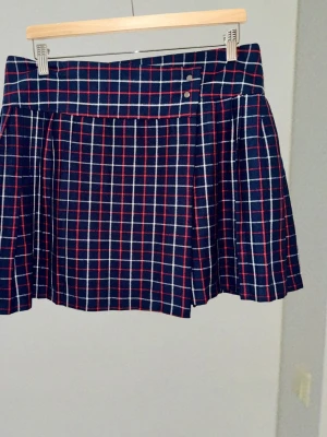 Rutig kilt-inspirerad kjol – Tidlös preppy-look L - Tidlös rutig kjol i mörkblått, rött och vitt! Snygg plisserad design nertill och dekorativa knappar i midjan för den rätta looken. Behagligt material med stretch och mjukt foder för perfekt passform och komfort. ​Märke: FB Sister ​Storlek: Large (Midja platt: 42 cm) ​Längd: 44 cm ​#fbsister #rutigkjol #preppy #plisserad #skoluniform #höstmode #storlekL #trend #rutigt #plick #foryou