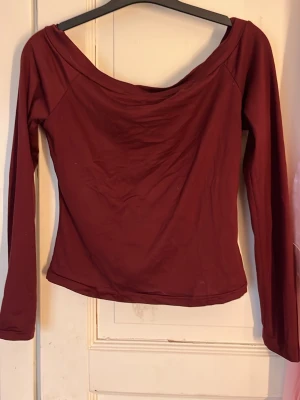 Vinröd offshoulder topp - Snygg vinröd offshoulder topp med långa ärmar. Toppen har en enkel, stilren design och är gjord i ett mjukt stretchigt material som sitter skönt på kroppen. Perfekt att styla med jeans eller kjol för en trendig look.