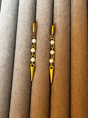 Guldörhängen med pärlor och spikes - Säljer ett par trendiga örhängen i guldton med små vita pärlor och spetsiga spikes längst ner. Örhängena har en cool kedjedesign och ger en edgy vibe till din look. Perfekta för dig som vill sticka ut med dina accessoarer.