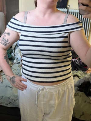 Randig off shoulder topp - Snygg ribbad off shoulder topp med marinblå och vita ränder. Croppad modell med bred krage som vilar på axlarna. Perfekt för en trendig och avslappnad look.