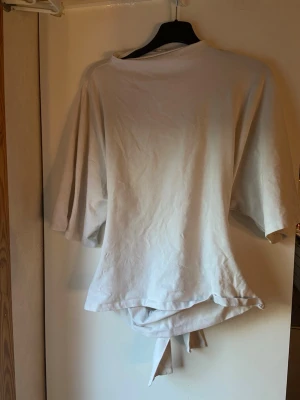 Vit topp med knytning i ryggen - En vit topp med knytning i ryggen. Har några få fläckar men som inte syns när man har den på sig💕