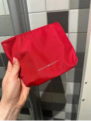 Röd necessär från Makeup Mekka - Snygg röd necessär från Makeup Mekka i slitstarkt tygmaterial. Perfekt för smink eller småprylar, med dragkedja upptill och enkel, stilren design. Logga i vitt framtill.