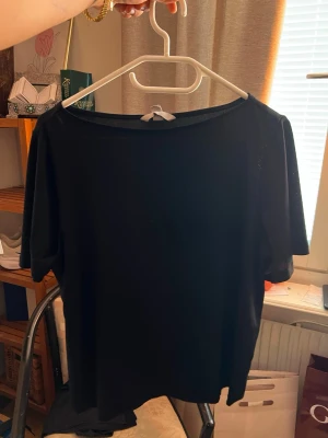 Svart t-shirt från H&M - En enkel svart t-shirt från H&M med rund halsringning och korta ärmar. Perfekt basplagg som är lätt att matcha med olika outfits. Tillverkad i mjukt och bekvämt material. Boatneck topp