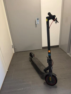 Svart Mi electric scooter PRO 2 Xiaomi - Elscooter i svart med röda detaljer och robust ram i metall. Utrustad med bred fotplatta, handtag med bra grepp och tydliga kablar. Perfekt för smidig transport i stan. Märket Xiaomi syns på styret. Laddare finns med också. Scootern har splitter nya bromsar och nytt broms handtag, även har jag köpt till ett nytt par massiva punkteringsfria däck. (Pris går att diskutera) Max fart 25km/h, räckvidd 30km utan extra batteri, 