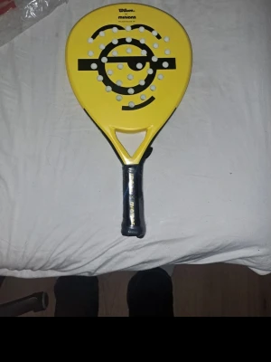 Wilson Minions padelracket gul - Säljer ett Wilson Minions padelracket i modellen Blade JR. Racketen är gul med svart Minions-motiv och har flera hål i bladet. Handtaget är svart med Wilson-tryck. Perfekt för dig som gillar padel och vill ha en unik design.