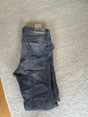 Grå raka jeans från Replay - Snygga grå jeans från Replay med raka ben och klassisk femficksmodell. Jeansen har en tvättad look med ljusare partier och tydliga sömmar. Perfekta för en avslappnad och trendig stil. Materialet är denim i bomull.