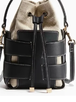 Svart och beige bucket bag i läder - Slutsåld Trendig bucket bag med svart läderdetaljer och beige canvas. Väskan har justerbar axelrem, dragskostängning med guldfärgade detaljer och kontrastsömmar. Perfekt för dig som gillar en modern och stilren look.