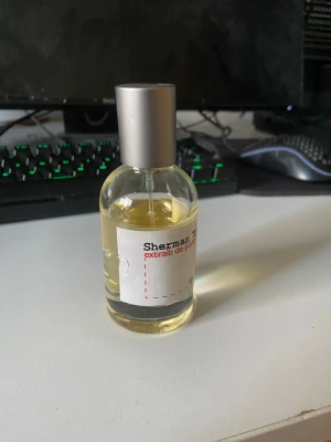 Oneboldchemist parfym - Sherman 78.0 extrait de parfum i en genomskinlig glasflaska med silverfärgad spraykork. Flaskan har en enkel vit etikett med svart och röd text. Parfymen har en ljusgul vätska och modern, minimalistisk design.