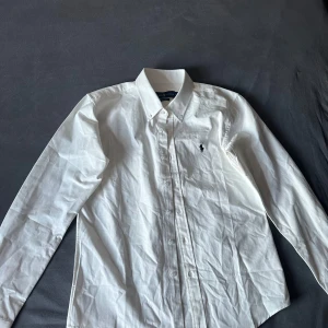 Vit skjorta från Ralph Lauren M - Klassisk vit Ralph Lauren-skjorta med ikonisk logga på bröstet. Perfekt för både vardag och fest – lite använd typ aldrig, tidlös och alltid rätt. Storlek M  🚀 Passa på innan den försvinner! 