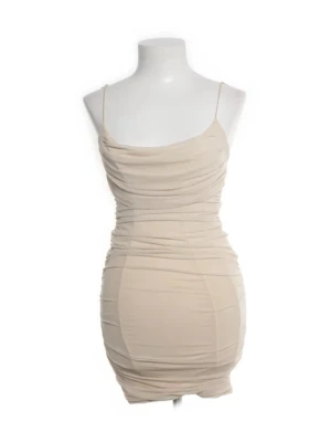 Klänning - Snygg beige kort klänning med tunna axelband och draperad effekt framtill. Klänningen har en kroppsnära passform och är perfekt för dig som gillar en stilren och trendig look. Tillverkad i ett mjukt och stretchigt material.