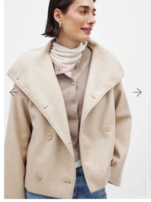 Beige ullkappa med stor krage - Snygg beige kappa med stor, bred krage och dubbelknäppning framtill. Kappan har en rak passform och stora knappar i matchande färg. Perfekt för dig som gillar en stilren och modern look.