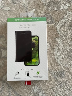 Svart läderfodral iPhone 14 Max - Snyggt och stilrent svart mobilskal i äkta full-grain läder från dbramante1928, designat för iPhone 14 Max. Fodralet har plats för upp till 5 kort och en notisficka, samt magnetiskt 2-i-1 wallet. Perfekt för dig som vill ha både skydd och funktion.