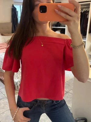 Röd offshoulder topp med volangärm - Trendig röd offshoulder topp med korta volangärmar. Toppen har en rak, croppad passform och är perfekt för dig som vill ha en enkel men snygg look. Tillverkad i ett mjukt och lätt material som känns skönt mot huden.