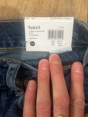 Blå tapered jeans från Taktíl - Snygga blå jeans från Taktíl i modellen William Tapered Mid Stone. Klassisk femficksdesign, normalhög midja och avsmalnande ben. Jeansen har en autentisk tvättad look och är perfekta för en avslappnad stil. Materialet är slitstarkt denim i bomull.