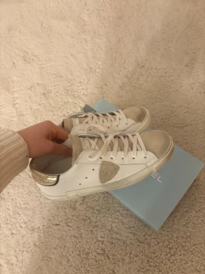 Vita Philippe Model skor - Snygga vita sneakers från Philippe Model med gulddetaljer på hälen och beige mocka. Klassisk låg modell med vita skosnören. Köpte i december men säljer nu då jag inte kan använda eftersom dom är för små💕 Köpta för 3500kr. Aldrig använda!!!! Köpta på Miinto 