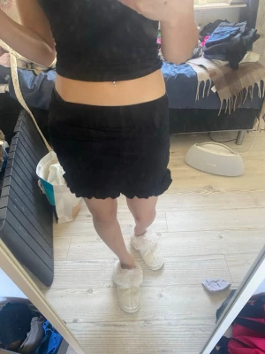 Svart volangkjol med scallop-kant - Säljer en svart kortkjol med volang och scallop-detaljer längst ner. Kjolen har en tight passform och är perfekt för dig som gillar en enkel men ändå söt stil. Materialet känns mjukt och stretchigt, vilket gör den bekväm att bära.