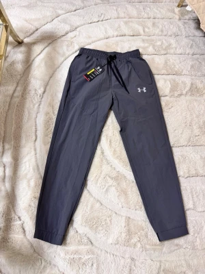 Under armour träningsbyxor - Snygga grå mjukisbyxor från Under Armour med resår i midjan och svarta dragsnören. Byxorna har raka ben, sidofickor och en vit logga på vänster lår. Perfekta för chill eller träning, tillverkade i ett lätt och mjukt material. Passar mer som S